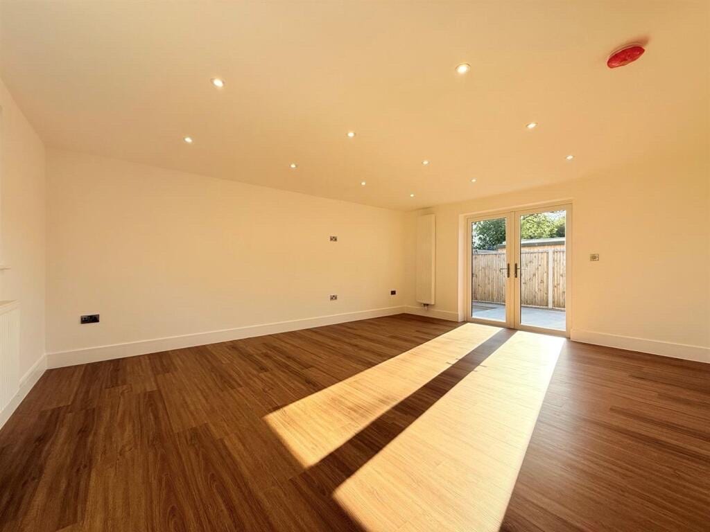 Dark oak LVT plank flooring in a large empty room, sunlight streaming through French doors onto a patio