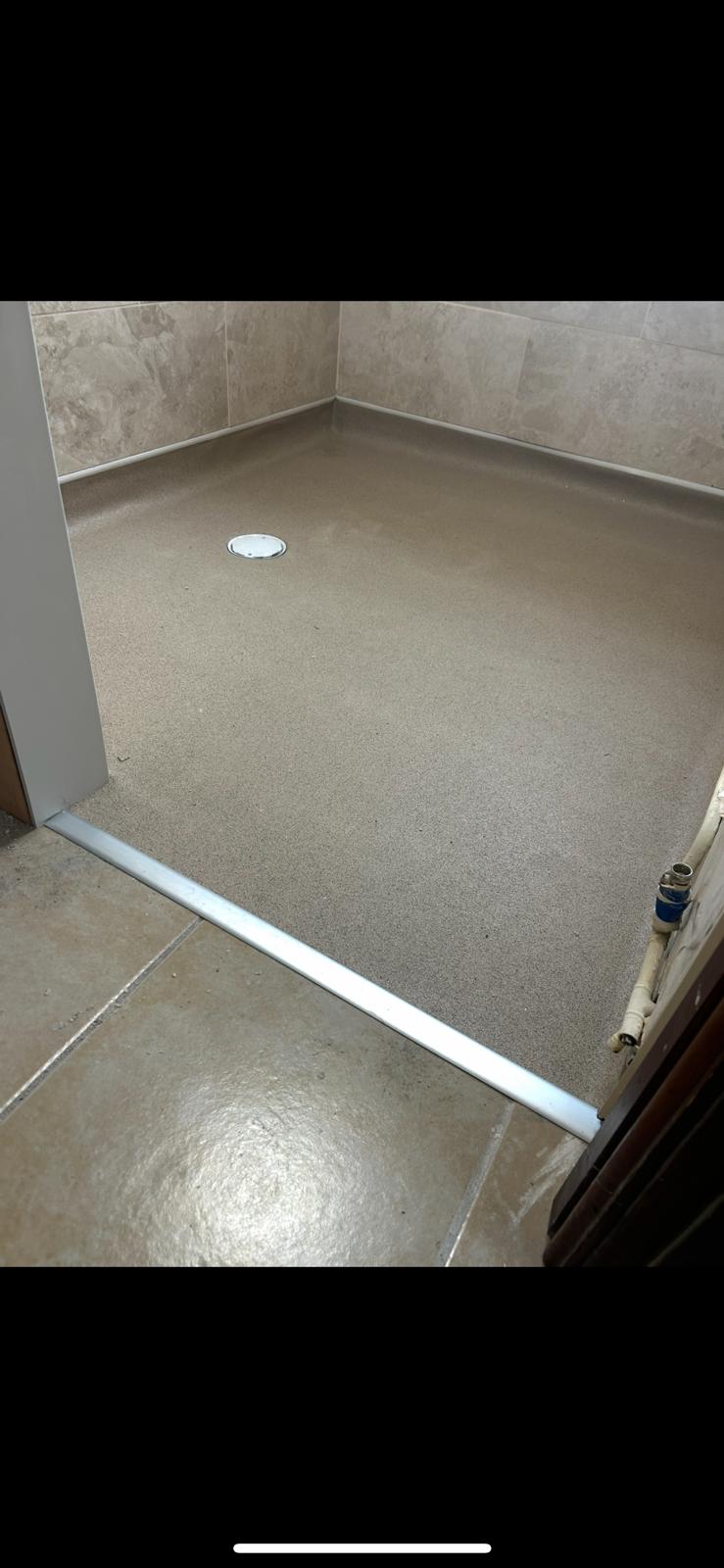 Beige cap-and-cove safety flooring with central gully drain fitted in a wet room by Compass Flooring Norfolk
