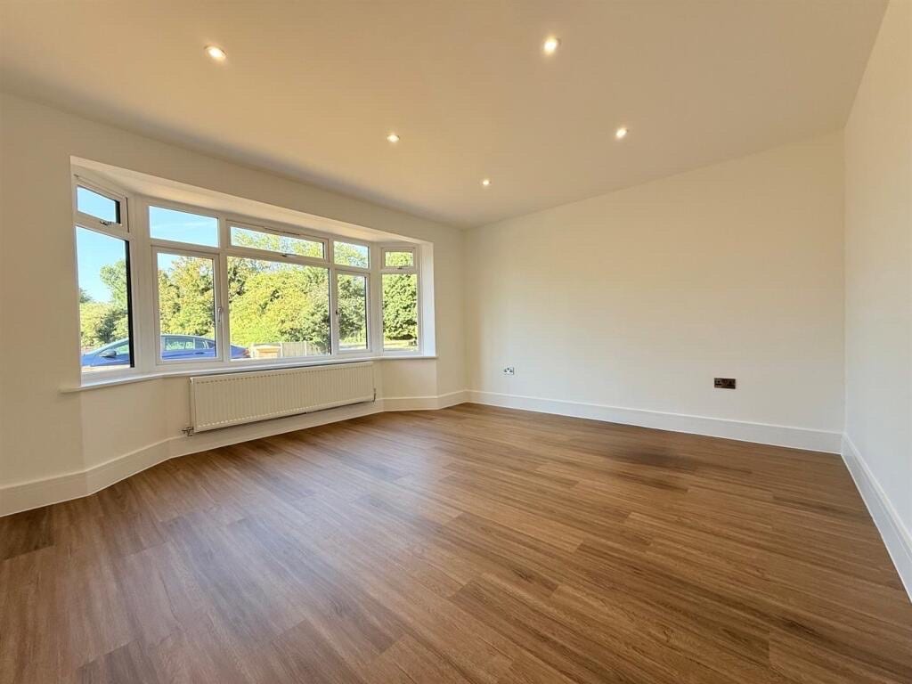 Mid-brown oak LVT plank flooring in an empty living room with a curved bay window overlooking trees