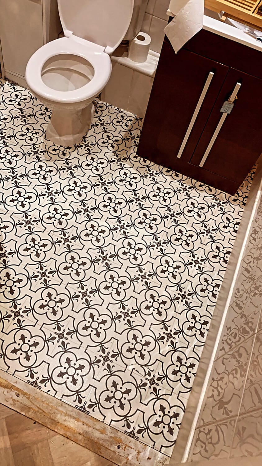 Monochrome Victorian tile-effect sheet vinyl fitted in a cloakroom, cut around the toilet pedestal and running to the doorway where it meets parquet flooring