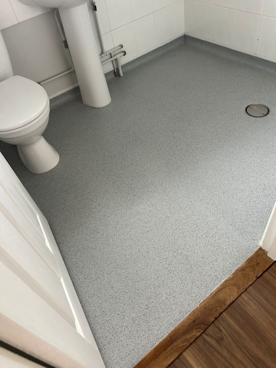 Slip-resistant grey wet room floor coved up the walls and finished flush at the doorway against wood-effect flooring, with no threshold to step over