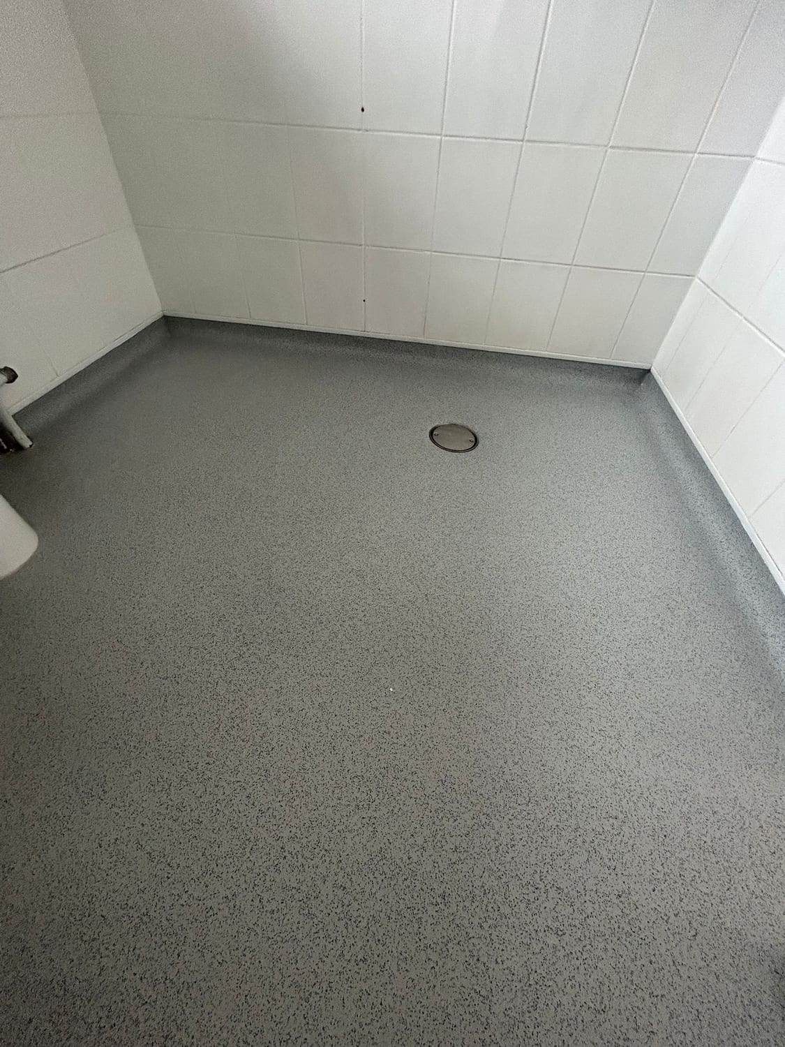 Close view of a welded safety vinyl wet room floor coved up to white tiled walls, laid to fall towards a clamped centre drain