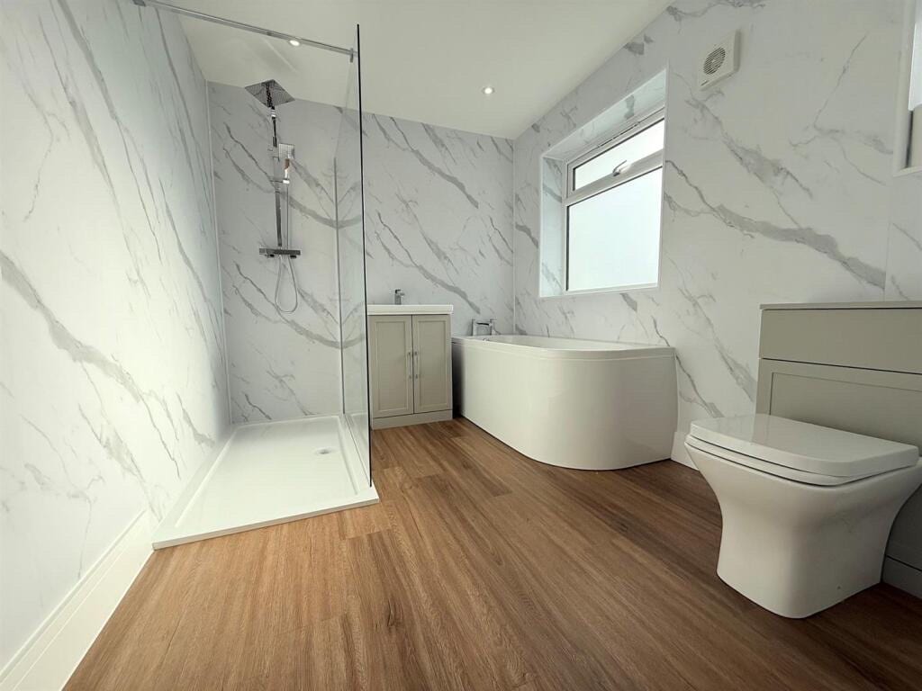 Warm oak wood-effect vinyl flooring in a bathroom with a walk-in shower, corner bath and marble-effect wall panels